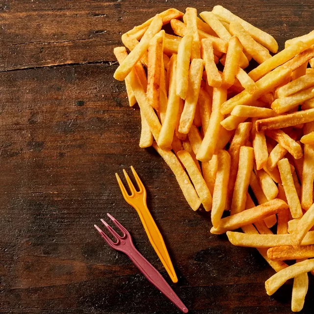 Ein Herz aus Pommes mit zwei Platikgabeln auf einer dunklen Holzunterlage