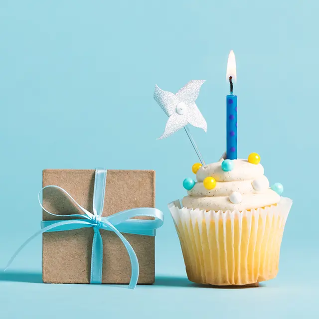 Ein Geschenk und ein Muffin mit Kerze auf einem hellblauen Hintergrund